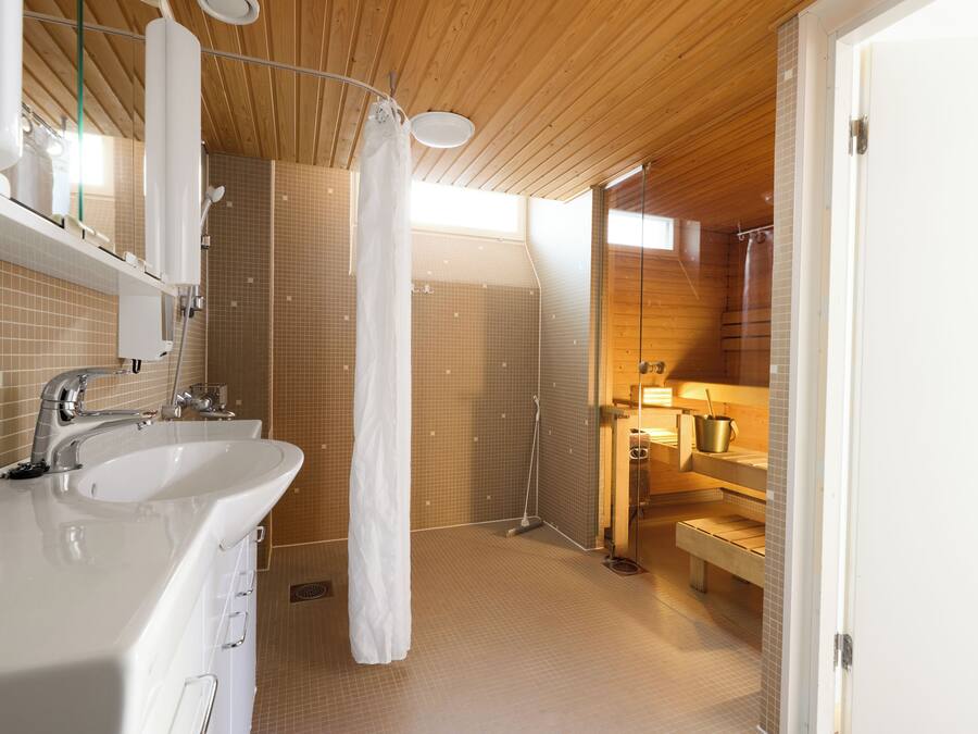 A modern bathroom with a wooden ceiling, a white sink, a shower with a curtain, and a bench.