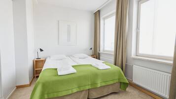 Un dormitorio ordenado con cama, mesitas de noche, un radiador y una ventana con cortinas.