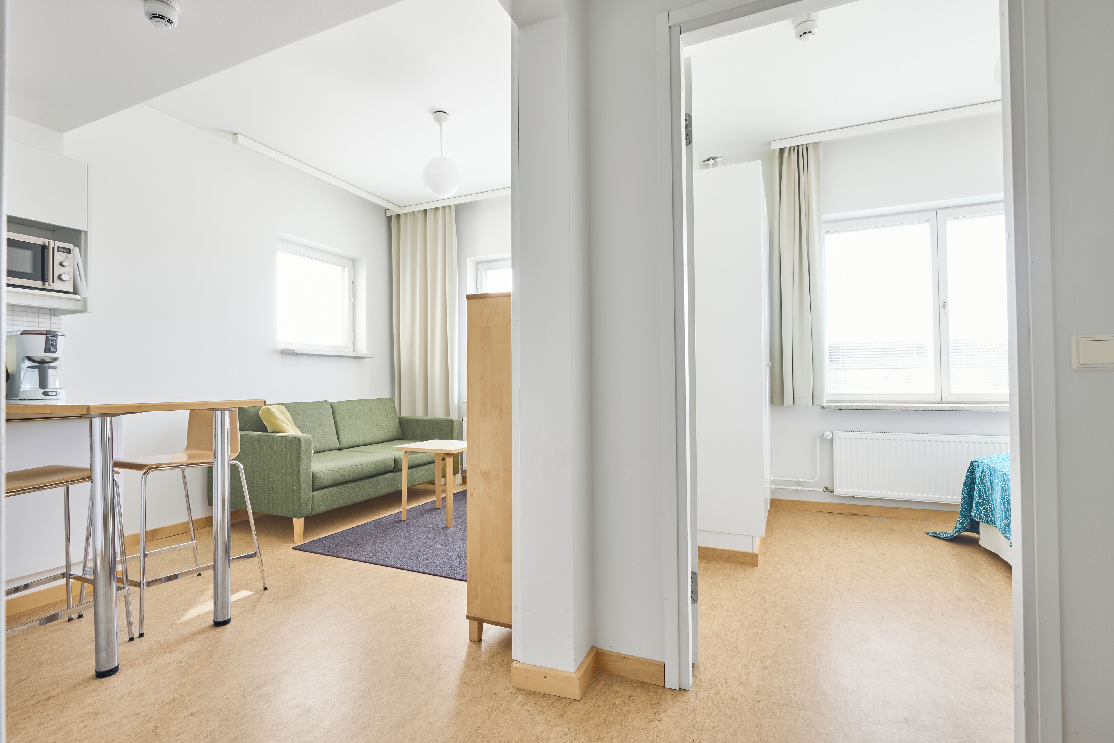 Eine moderne Wohnung mit einer Küchenzeile, einem grünen Sofa, einem Holztisch und Blick ins Freie.