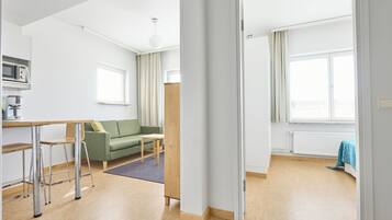 Eine moderne Wohnung mit einer Küchenzeile, einem grünen Sofa, einem Holztisch und Blick ins Freie.