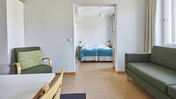 A room with a green sofa, a wooden chair, a small table, and a bed with blue bedding.