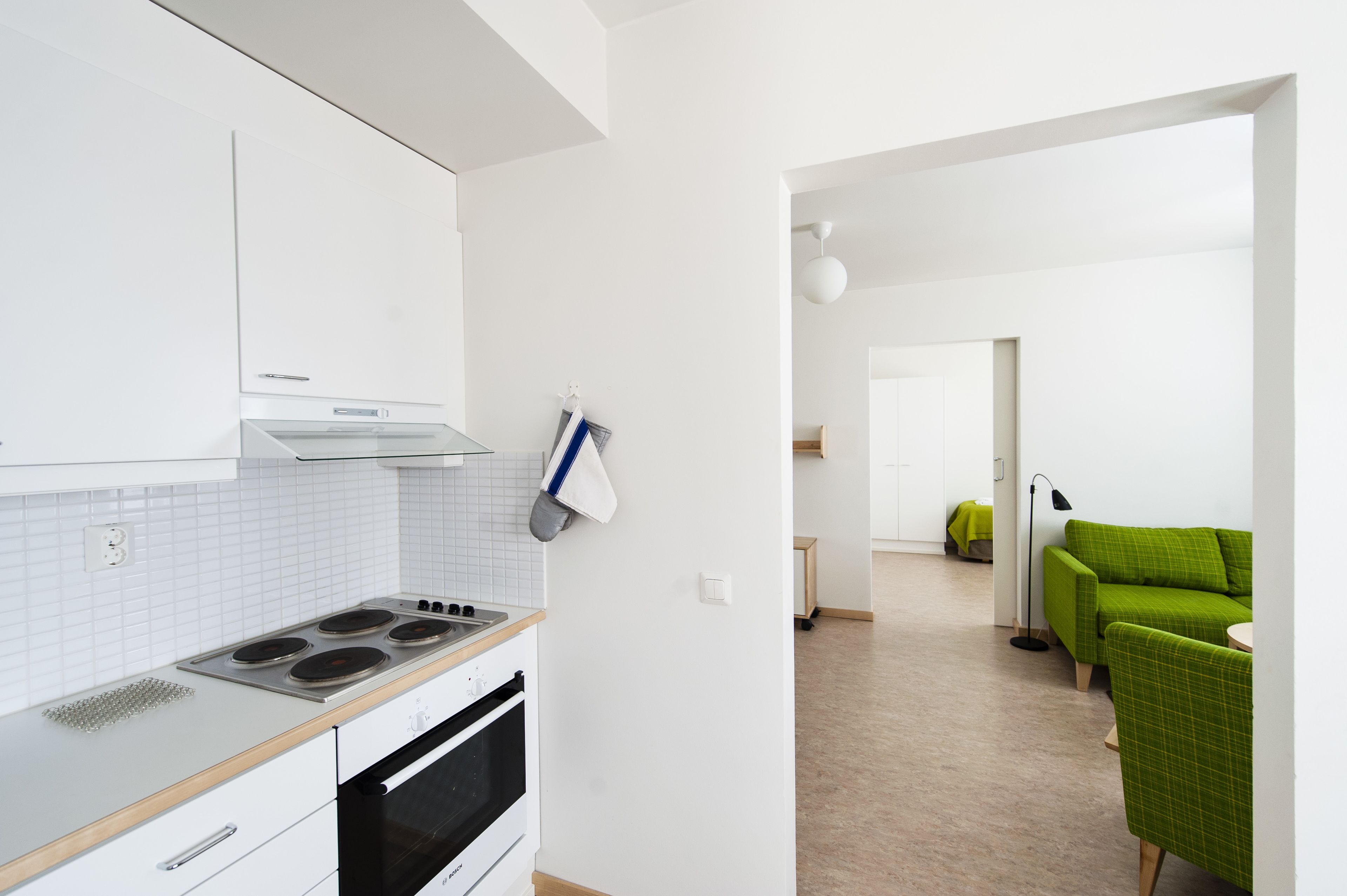 Una cocina moderna con armarios blancos, una estufa y una encimera. En la zona de estar contigua hay un sofá verde y una mesita.