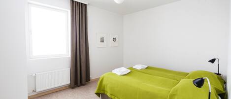 A hotel room with a bed, a nightstand, a lamp, a window with curtains, and a radiator.