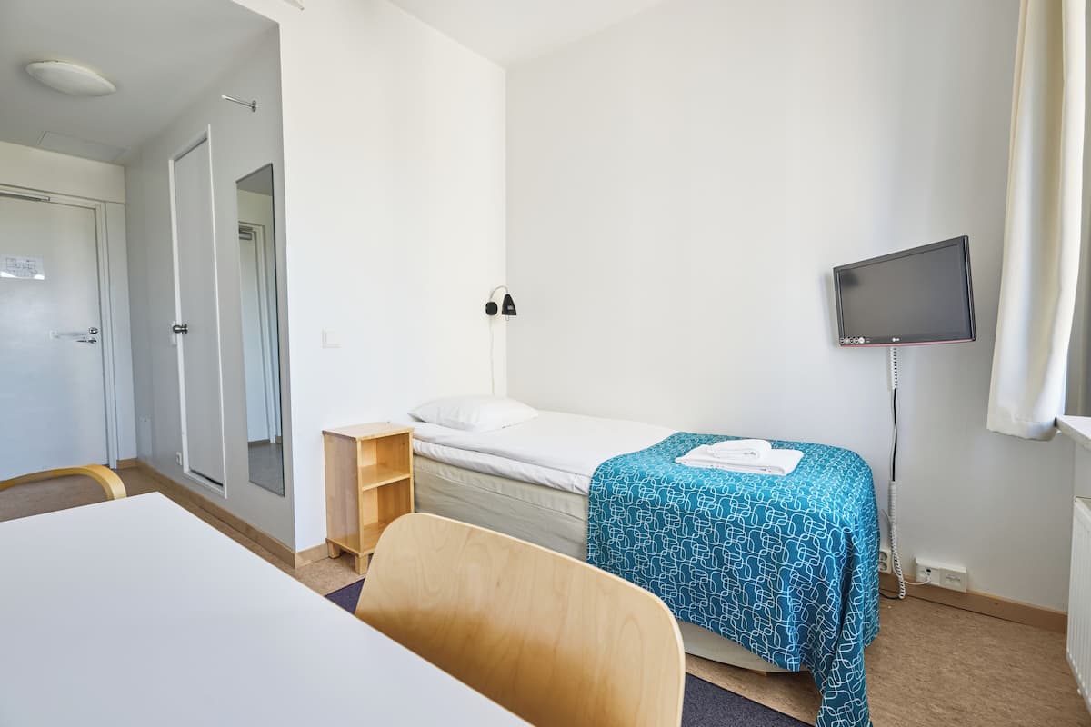 A hotel room with a bed, a desk, a chair, a TV, and a door.