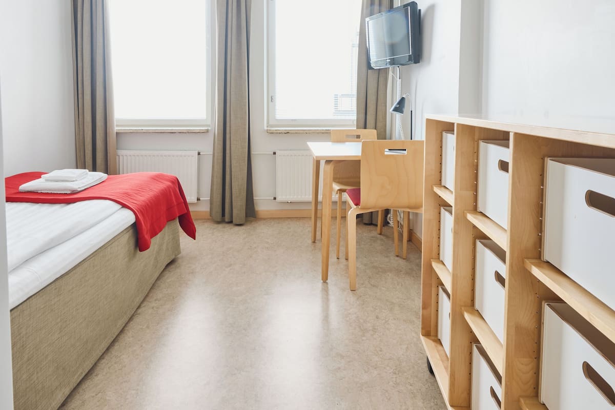 A hotel room with a bed, a desk, a television, and storage units.