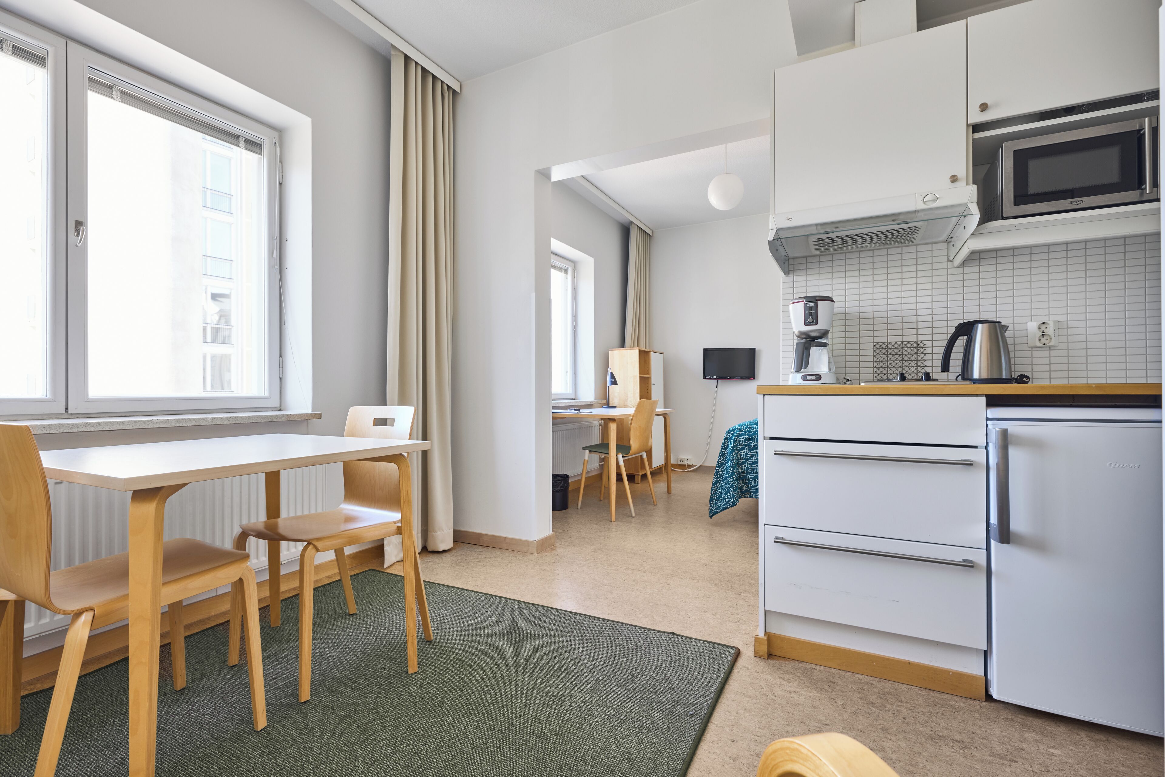 A modern kitchen with white cabinets, a microwave, a coffee maker, and a refrigerator. There is a dining area with a table and chairs.