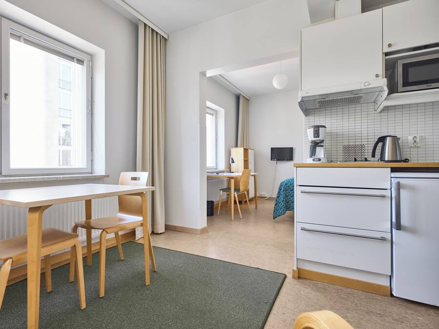 A modern kitchen with white cabinets, a microwave, a coffee maker, and a refrigerator. There is a dining area with a table and chairs.