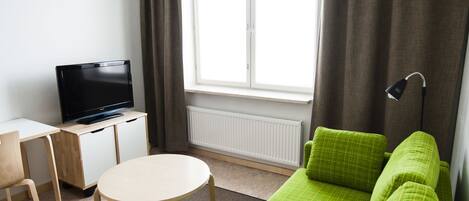 Un salon moderne avec un canapé vert, un téléviseur posé sur un meuble en bois, une table ronde et une grande fenêtre avec des rideaux.