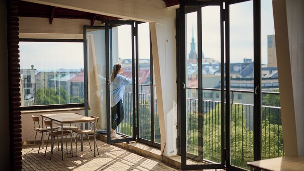 A balcony with a table and chairs, a view of buildings and greenery, and a person opening a door. - Töölö Towers (Helsinki)