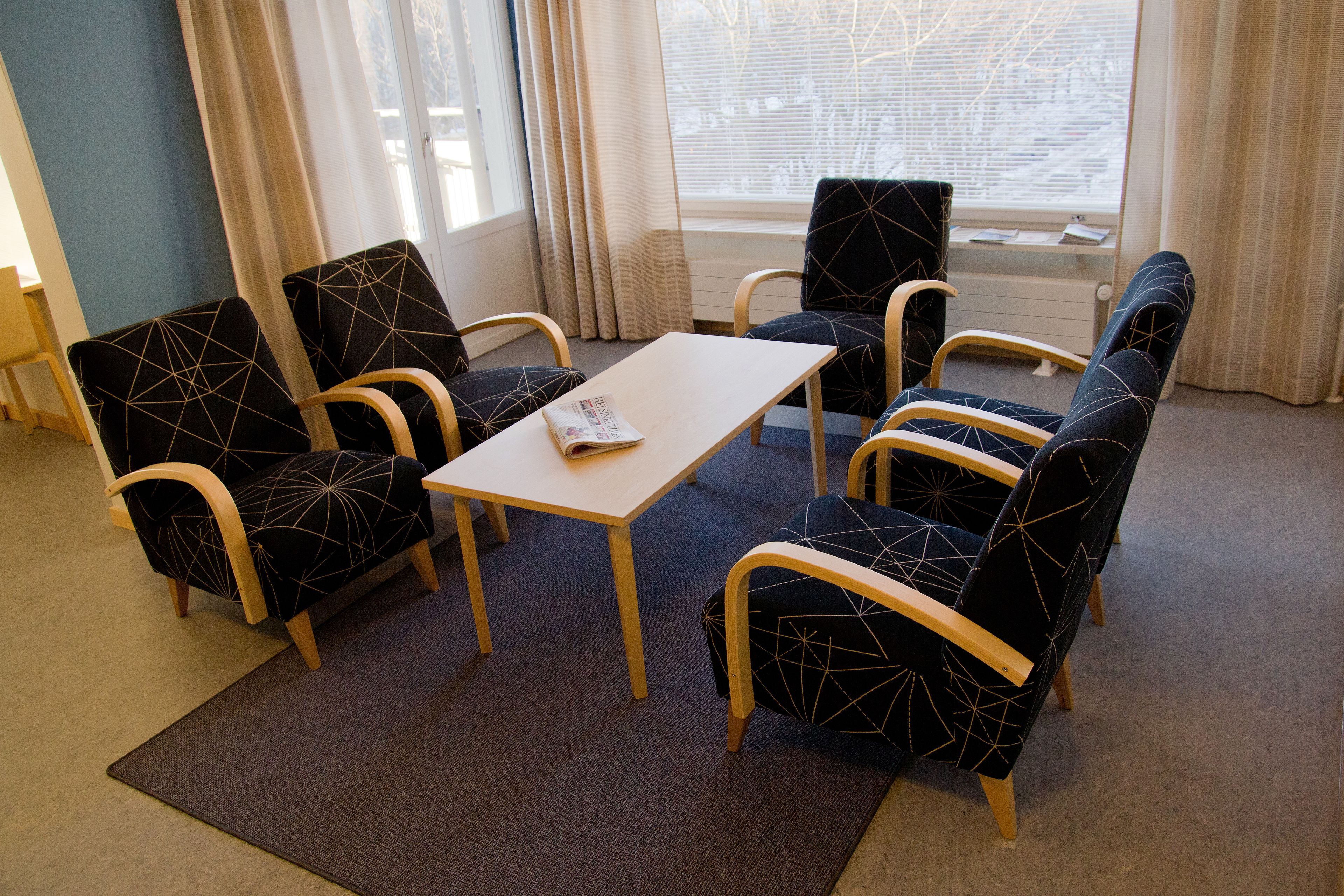 A room with a table and four chairs with geometric patterns, a window with curtains, and a view of the outside.