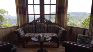 Una habitación con un sofá a rayas de cebra, una mesa redonda de madera con una tetera y una taza, y vistas a un paisaje verde a través de ventanas amplias.