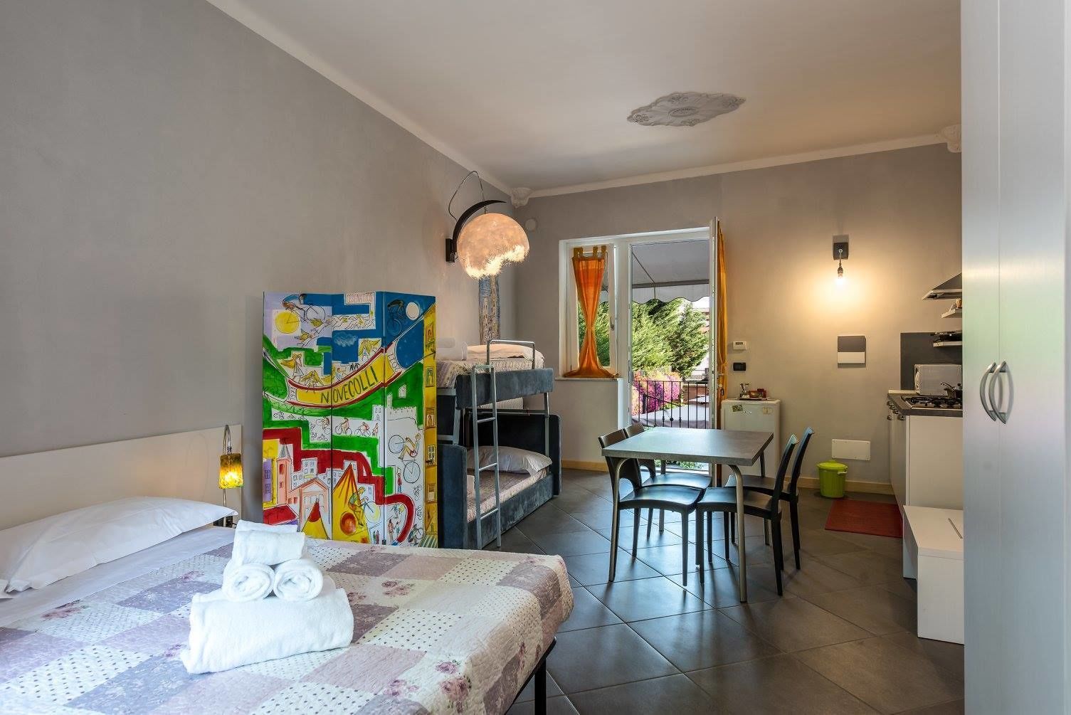 A compact hotel room with a bed, a dining table, and a kitchenette.