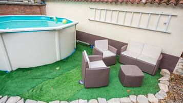 Patio esterno con piscina, mobili in vimini e tetto in tegole.