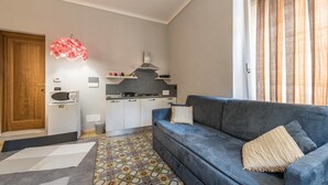 Een compacte woonruimte met een kitchenette, een blauwe bank en een kamerkleed met een patroon.