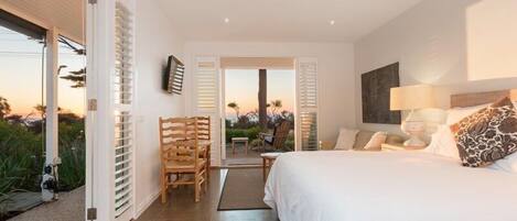 A bedroom with a bed, a nightstand, a lamp, and a view of the outdoors.