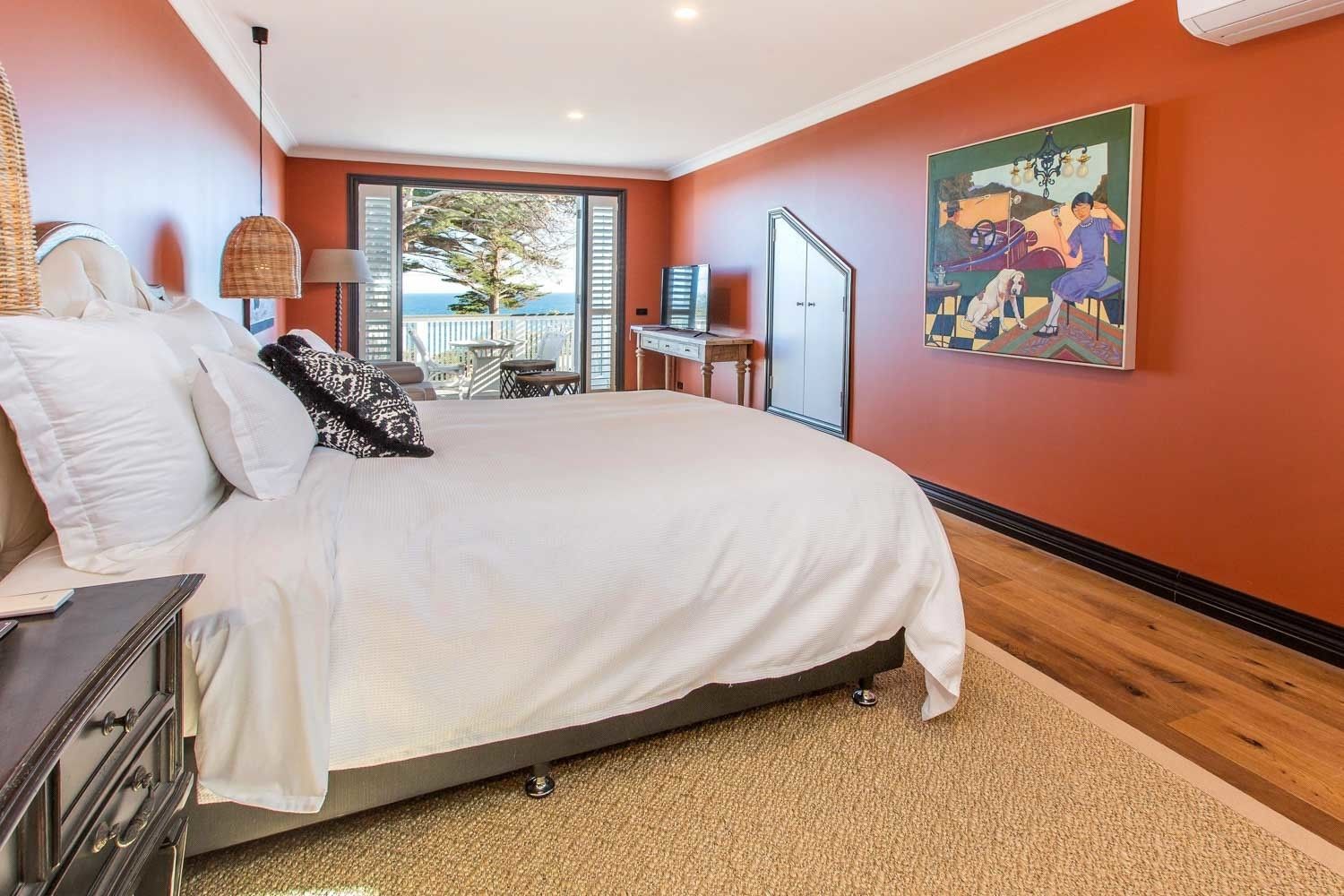 A bedroom with a large bed, a desk, and a painting on the wall.