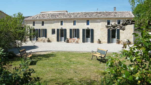 Un bâtiment en pierre avec un toit en tuiles, de nombreuses fenêtres dotées de volets et des sièges à l’extérieur.