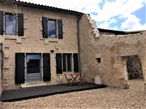 A rustic building with a stone facade, multiple windows with shutters, and a small outdoor seating area with a table and chairs. - Clos Vieux Rochers (Puisseguin)
