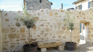Un mur de pierre agrémenté de deux oliviers en pot et d’un banc en pierre.