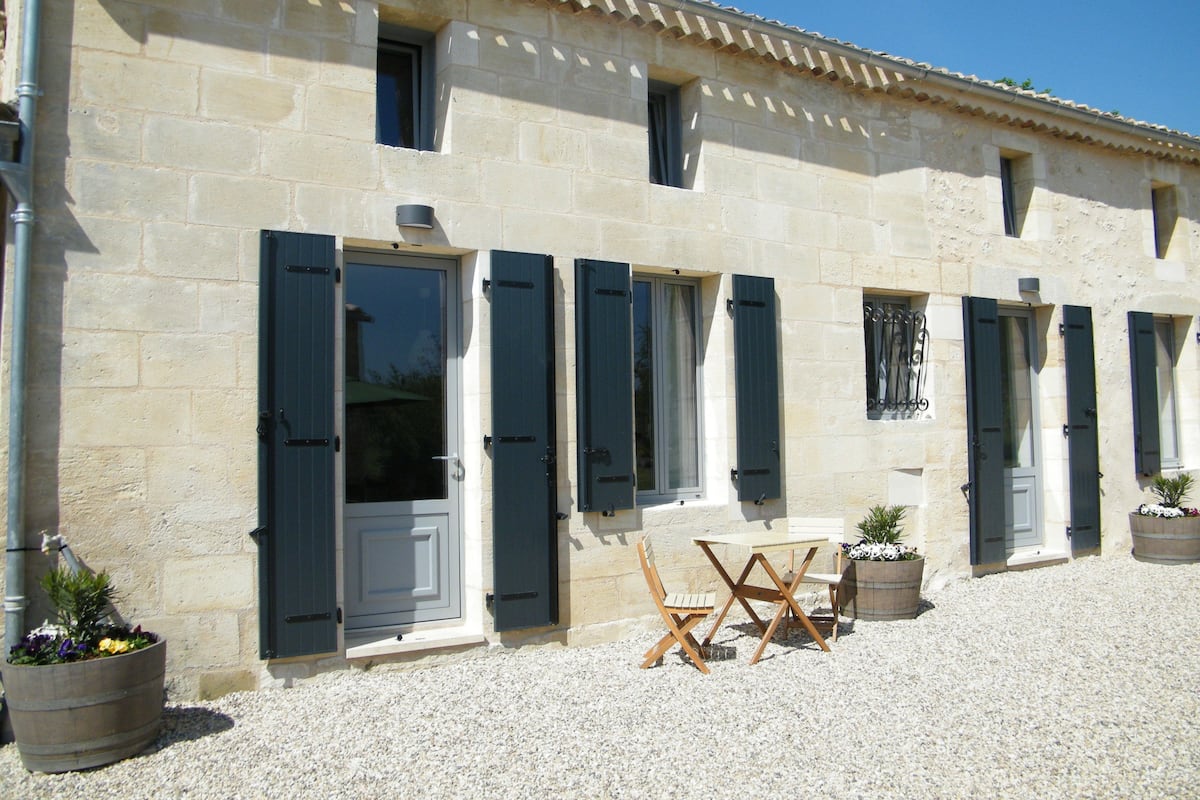 A stone building with multiple windows and doors, outdoor seating, and potted plants.