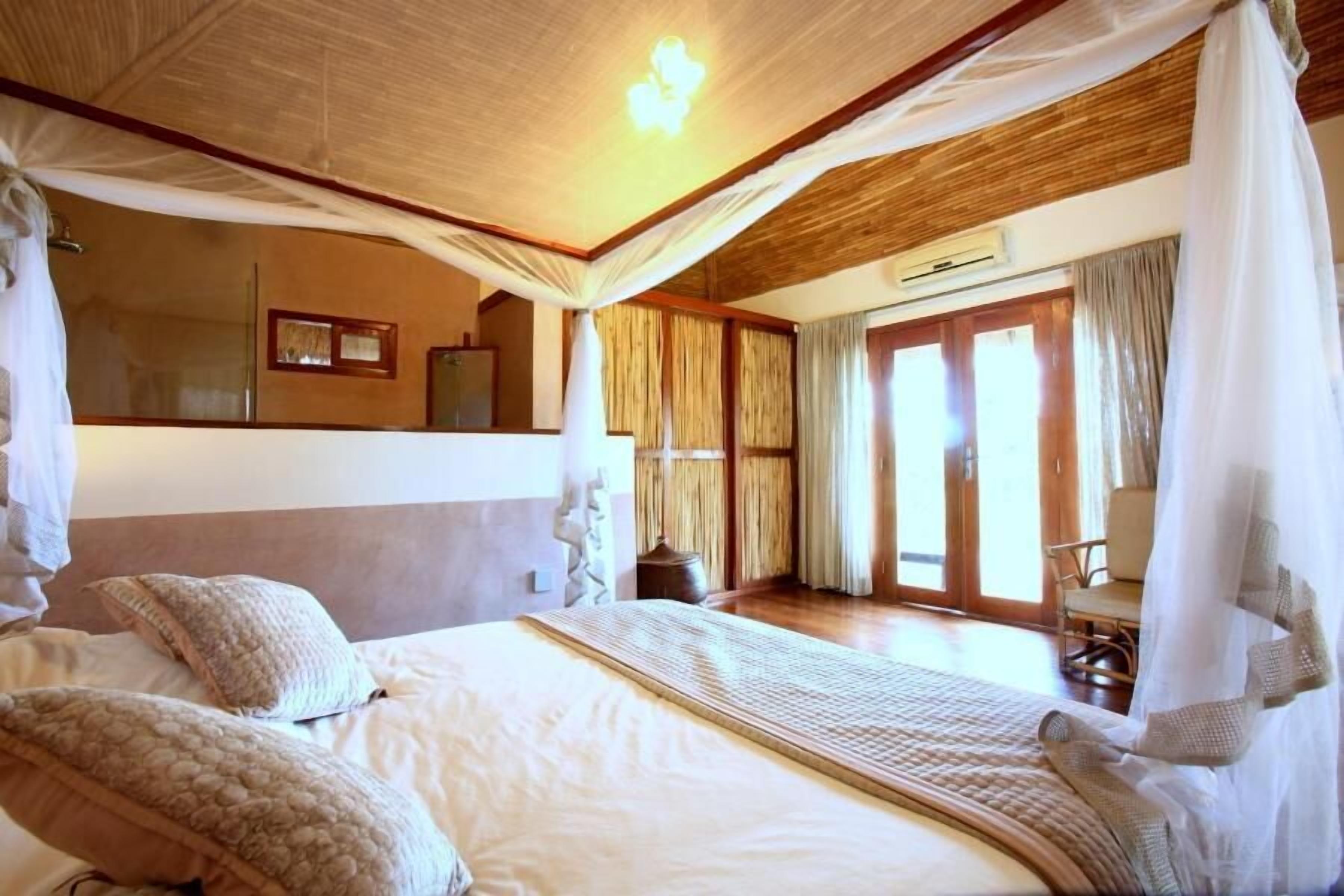 A bedroom with a large bed, canopy, and a view of the outdoors.