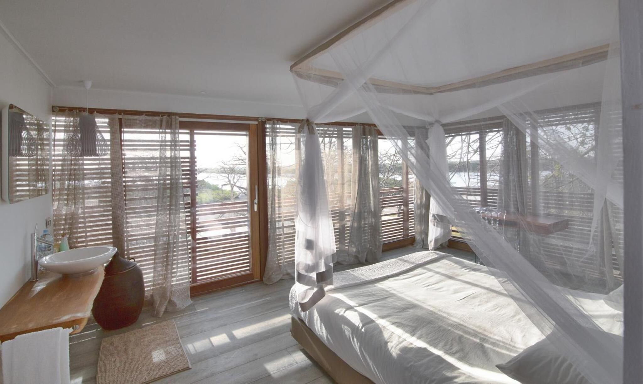 A bedroom with a large bed, a bedside table, a mirror, and a window with blinds.