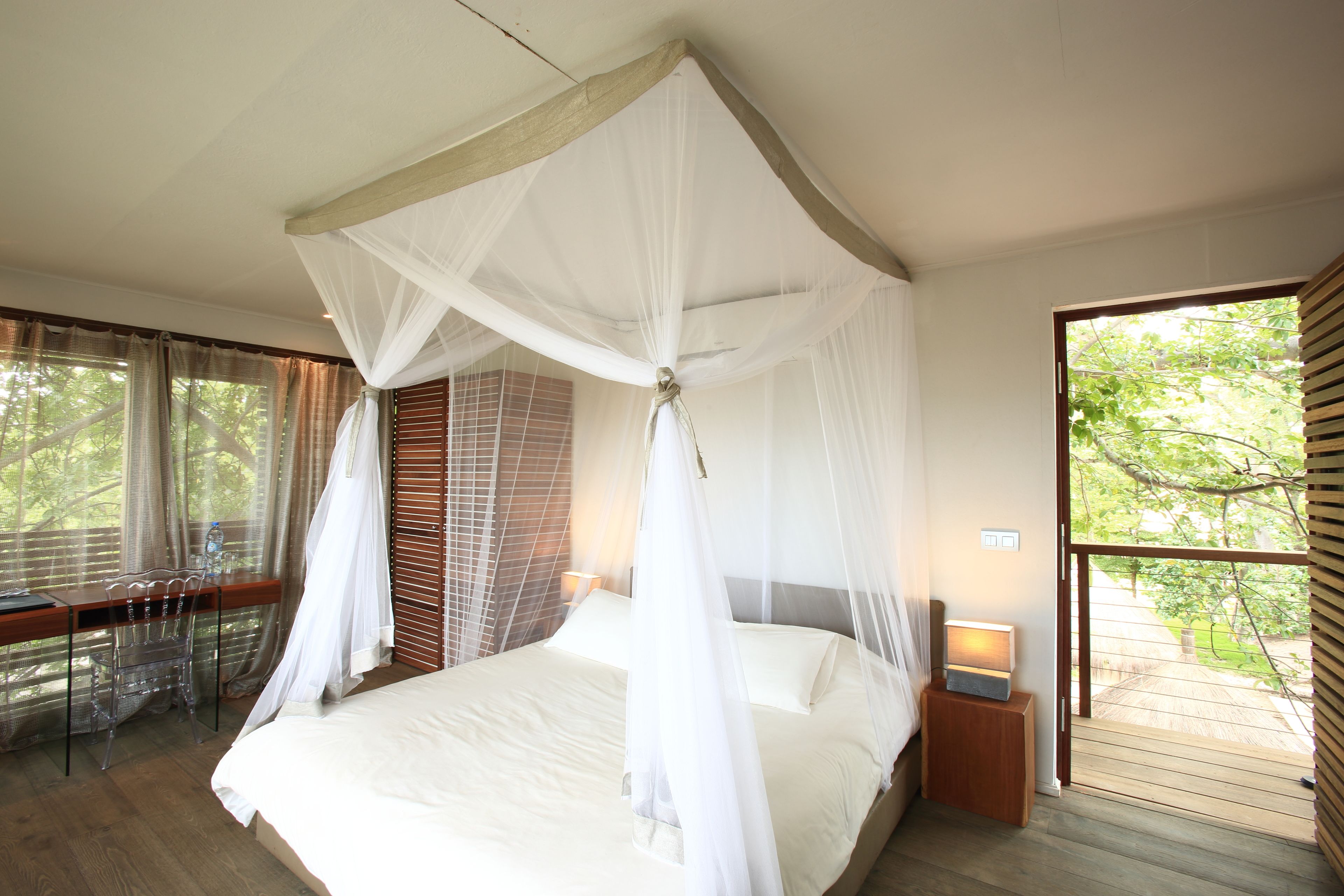 Un dormitorio con cama con dosel, un escritorio con sillas y vistas al exterior.