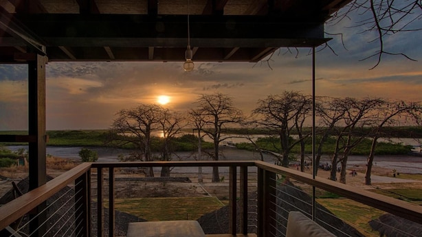 Una terraza de madera con vista a la puesta de sol sobre un río y árboles.
