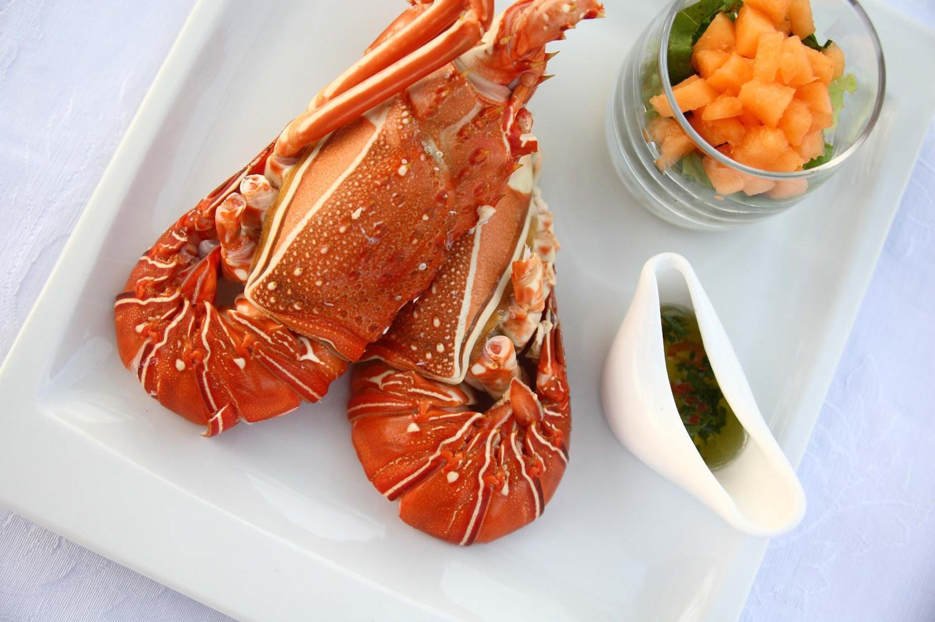 Un langostino en un plato blanco, acompañado de verduras picadas y un recipiente pequeño con salsa.