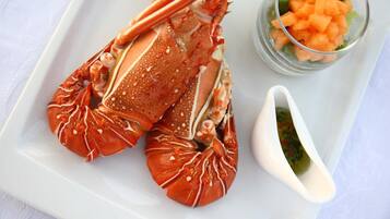 Un langostino en un plato blanco, acompañado de verduras picadas y un recipiente pequeño con salsa.