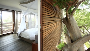 Un dormitorio con una cama grande, un muro de listones de madera y un árbol que crece a través de la pared.