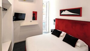 A modern hotel room with a large bed, a mounted TV, a red accent wall, and a view of the city through the window. - Art Street Hotel (Naples)