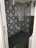 Un angolo doccia con parete in piastrelle decorate, una porta in vetro e un lavandino bianco.