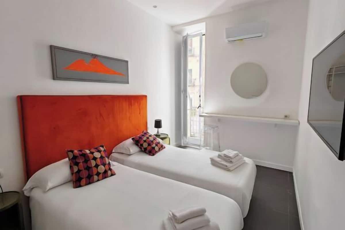 A hotel room with two beds, a large mirror, a painting, and a window.