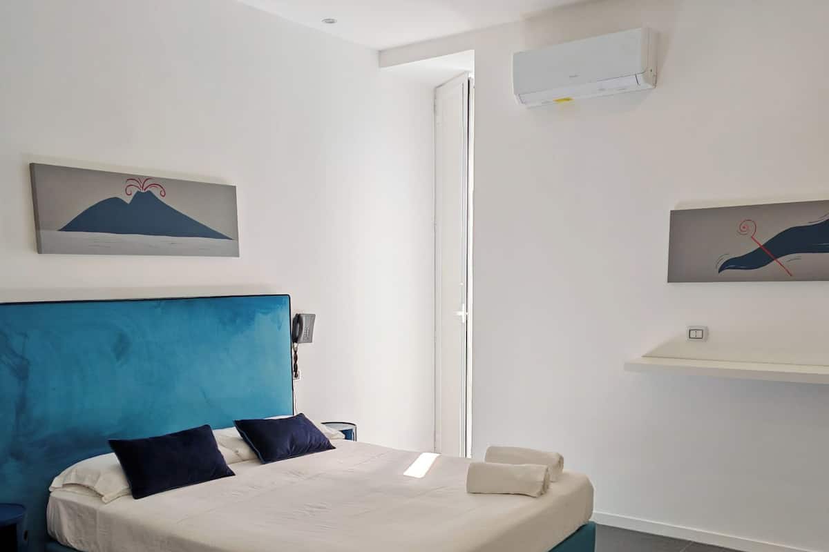 A bedroom with a bed, a blue headboard, a white wall, and a door.