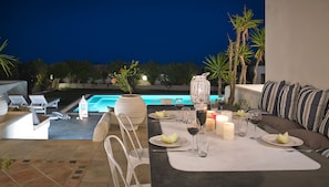 An outdoor dining area with a pool view, white furniture, and candles. - Aleria Villa (Santorini)