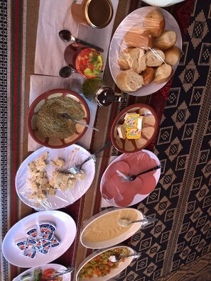 A table with various food items and condiments, including a plate of bread, a bowl of soup, and a plate of meat.