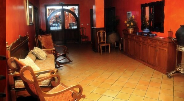Una habitación con sofá de madera, mecedoras, piso de baldosas y un mueble de madera con espejo.