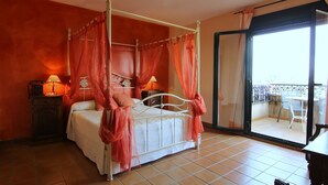 Una cama con dosel, una mesita de noche con lámpara y vistas al balcón exterior a través de un ventanal.