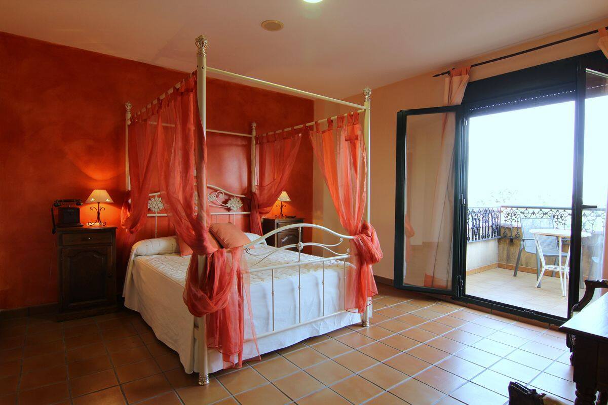 A four-poster bed with a canopy, a nightstand with a lamp, and a view of the outdoor balcony through a glass door.