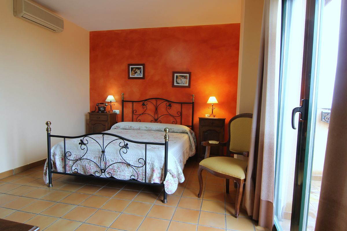 Une chambre à coucher avec un lit, deux tables de chevet, une chaise et une fenêtre avec des rideaux.