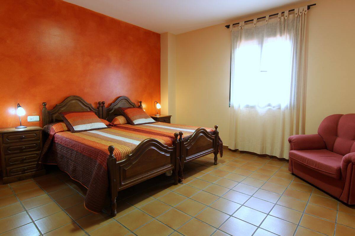 A bedroom with a wooden bed, two bedside tables, a red chair, and a window with curtains.