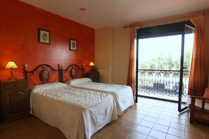Habitación de hotel con dos camas, un balcón con barandilla metálica y vistas al exterior.