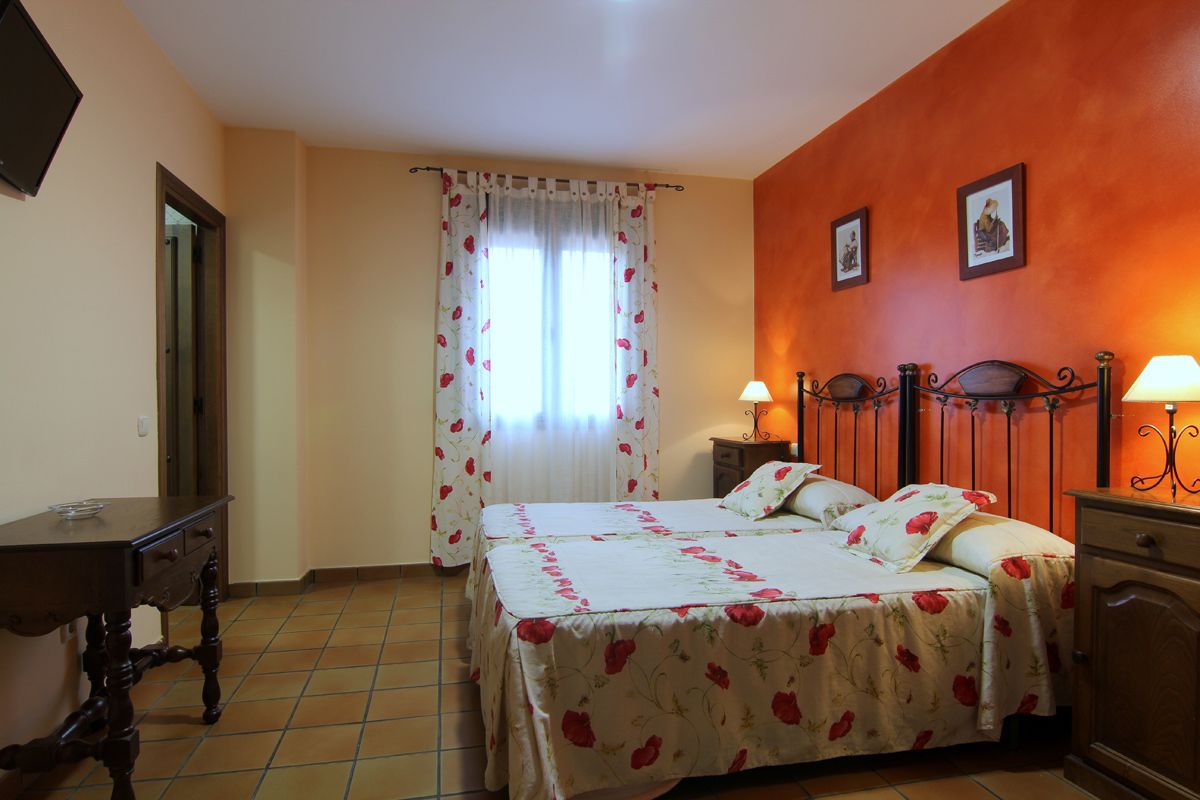 A bedroom with a bed, bedside tables, a nightstand, a dresser, and a window with curtains.