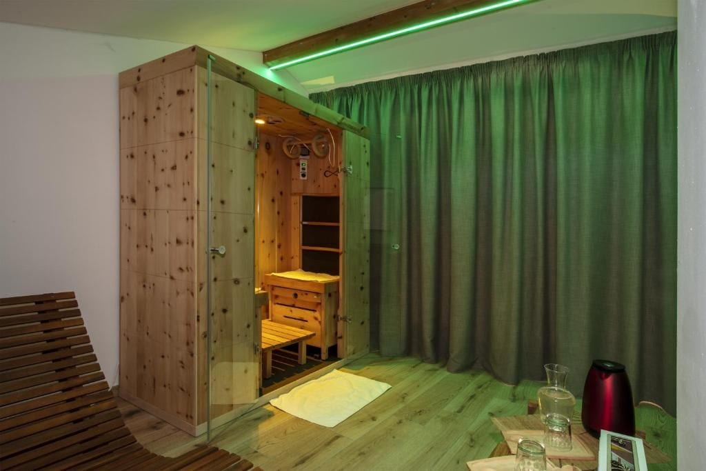 A wooden room with a glass door leading to a sauna area, a bed, and a table with a red vase.