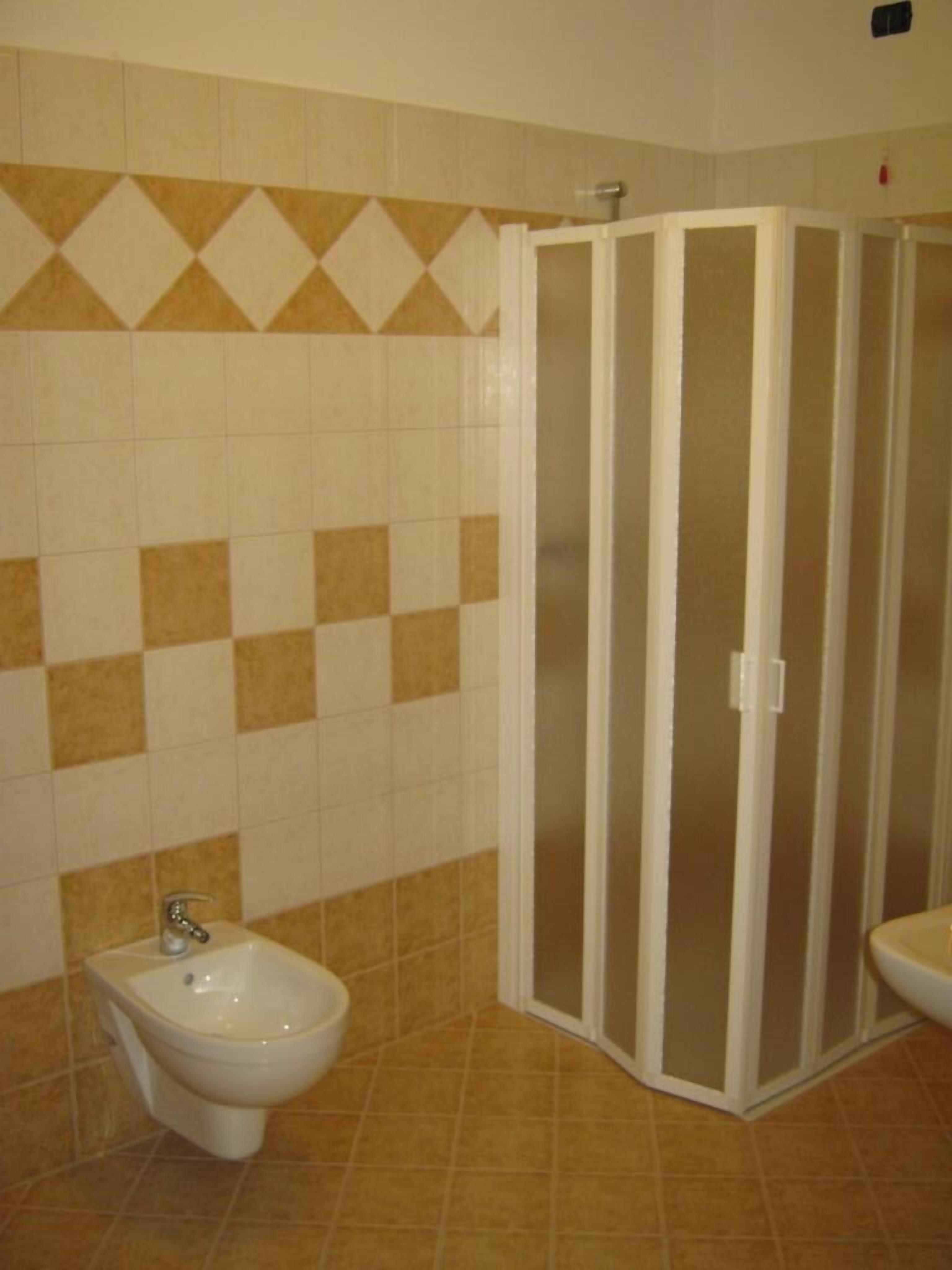 Un bany amb un paviment de quadrícula, un vàter blanc i un espai de dutxa blanc.