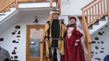 Un uomo e una donna in costumi d'epoca davanti a un edificio con una scala di legno e pareti in pietra.