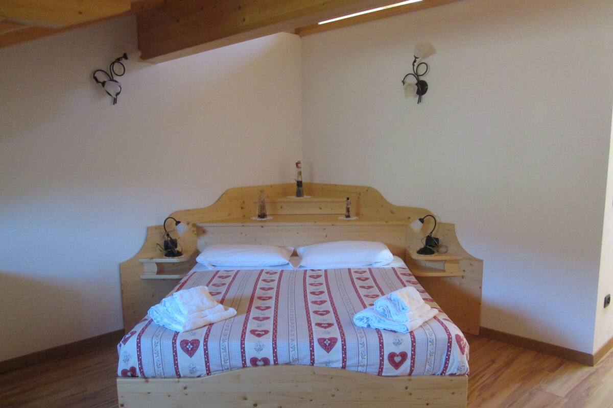 A wooden bed with a heart-patterned bedspread, two bedside tables with lamps, and a wooden headboard.