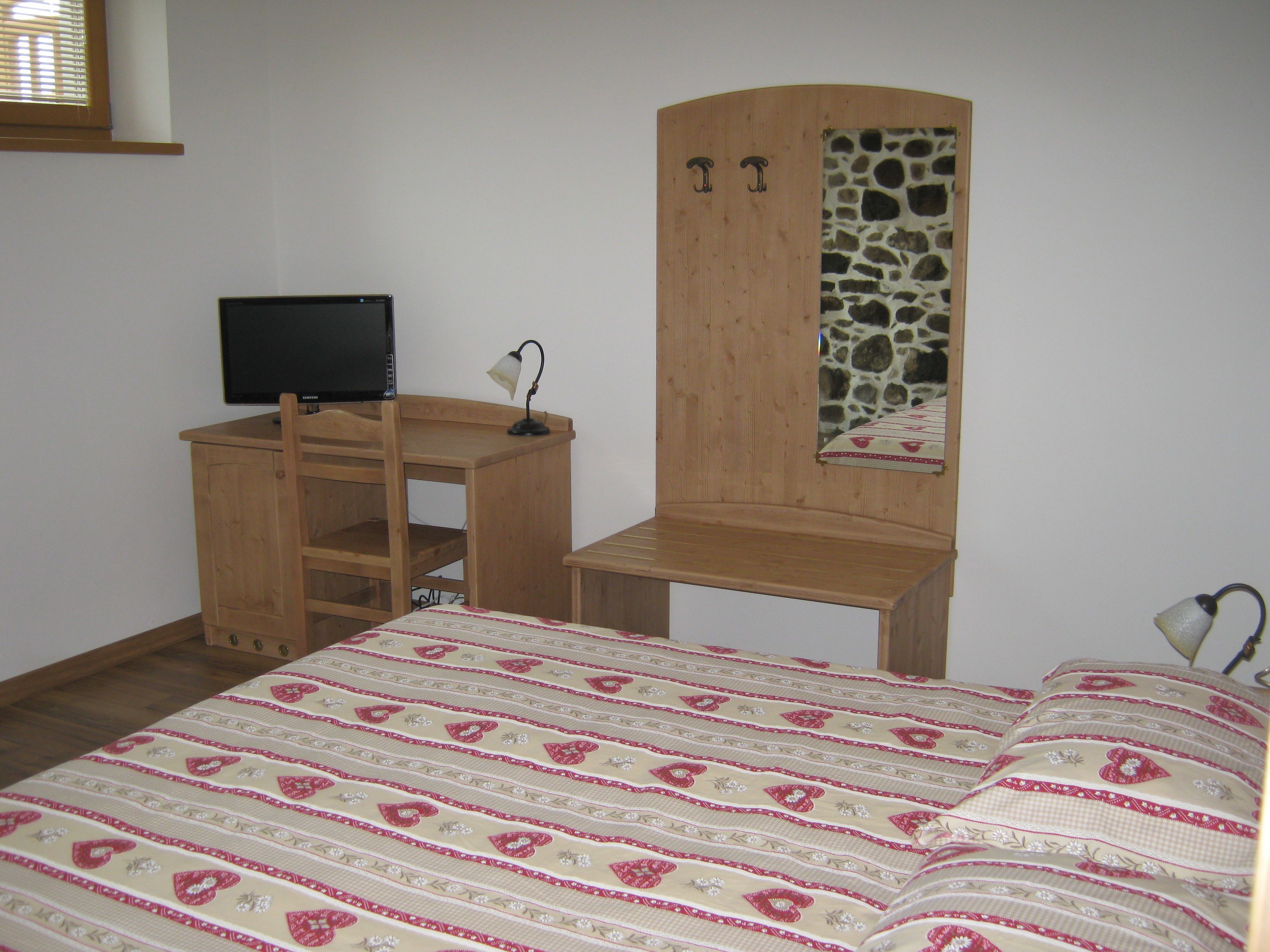 A bedroom with a bed, a desk, a chair, a television, and a stone wall.