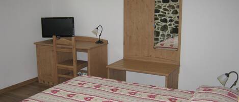 A bedroom with a bed, a desk, a chair, a television, and a stone wall.